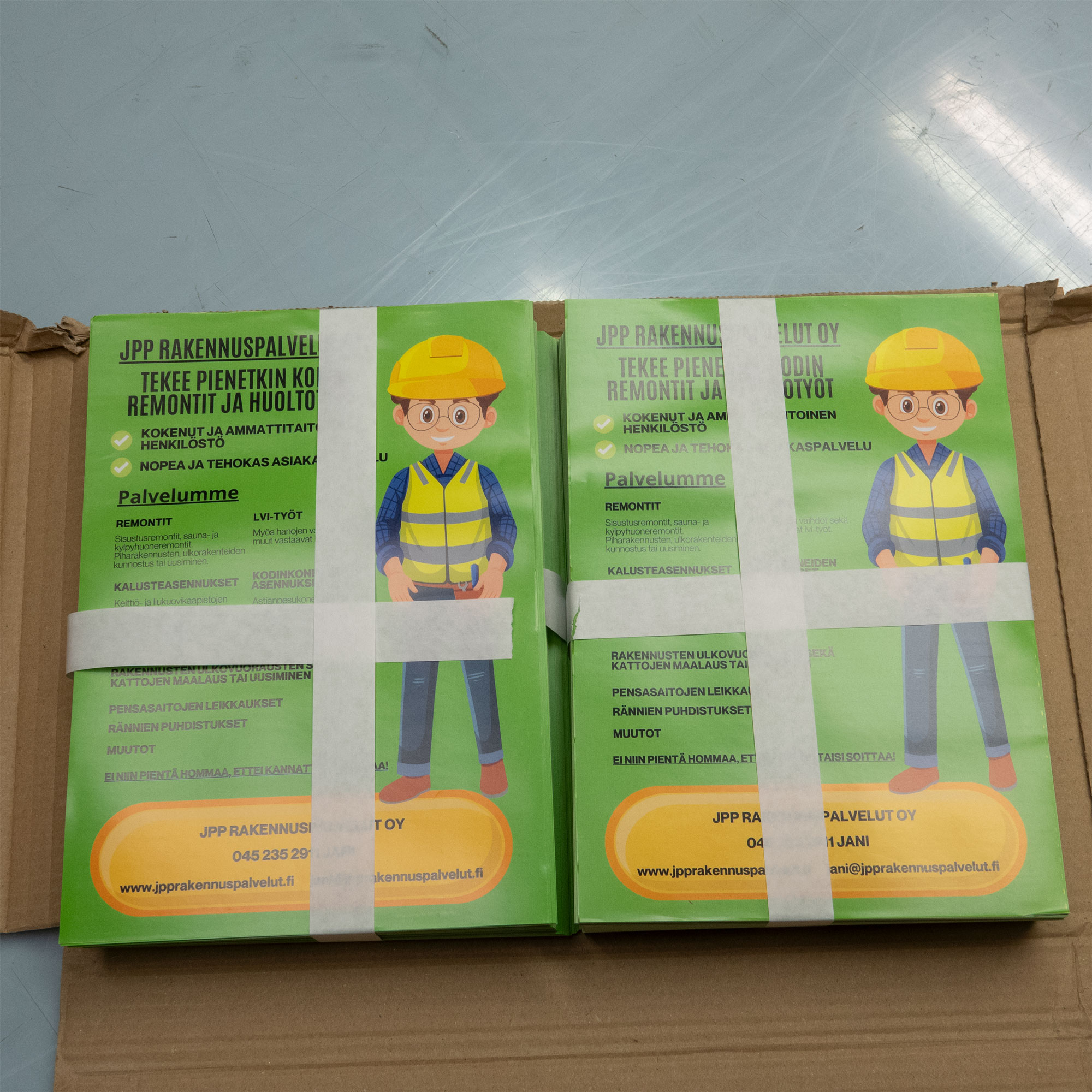 Digipainotuote kuva, kasa esitteitä pahvilaatikon päällä.